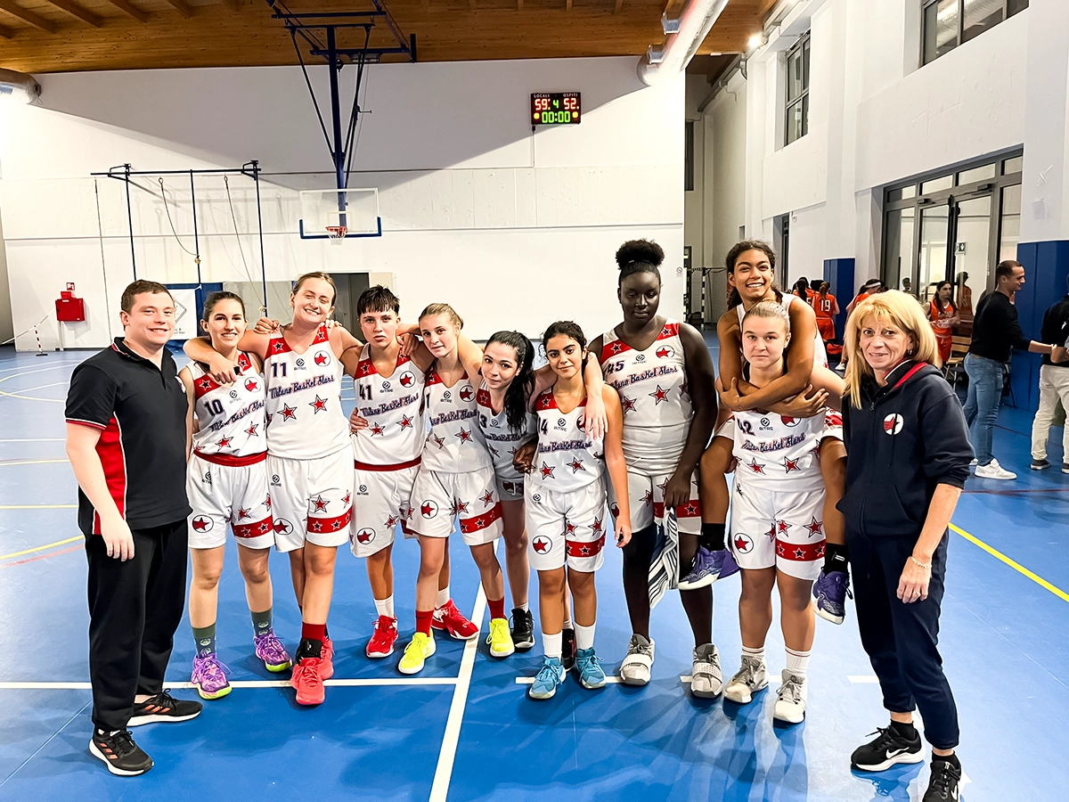 La squadra U17 di Milano Basket Stars festeggia la vittoria contro Ardor Bollate con il punteggio di 59-52. Le giocatrici e lo staff posano sorridenti sul campo di basket.